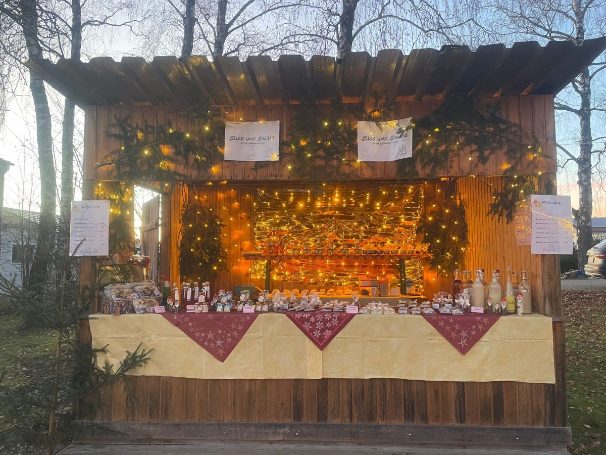 Weihnachtlich geschmückter Holzstand mit Tannengrün, Lichterketten und selbstgemachten Leckereien