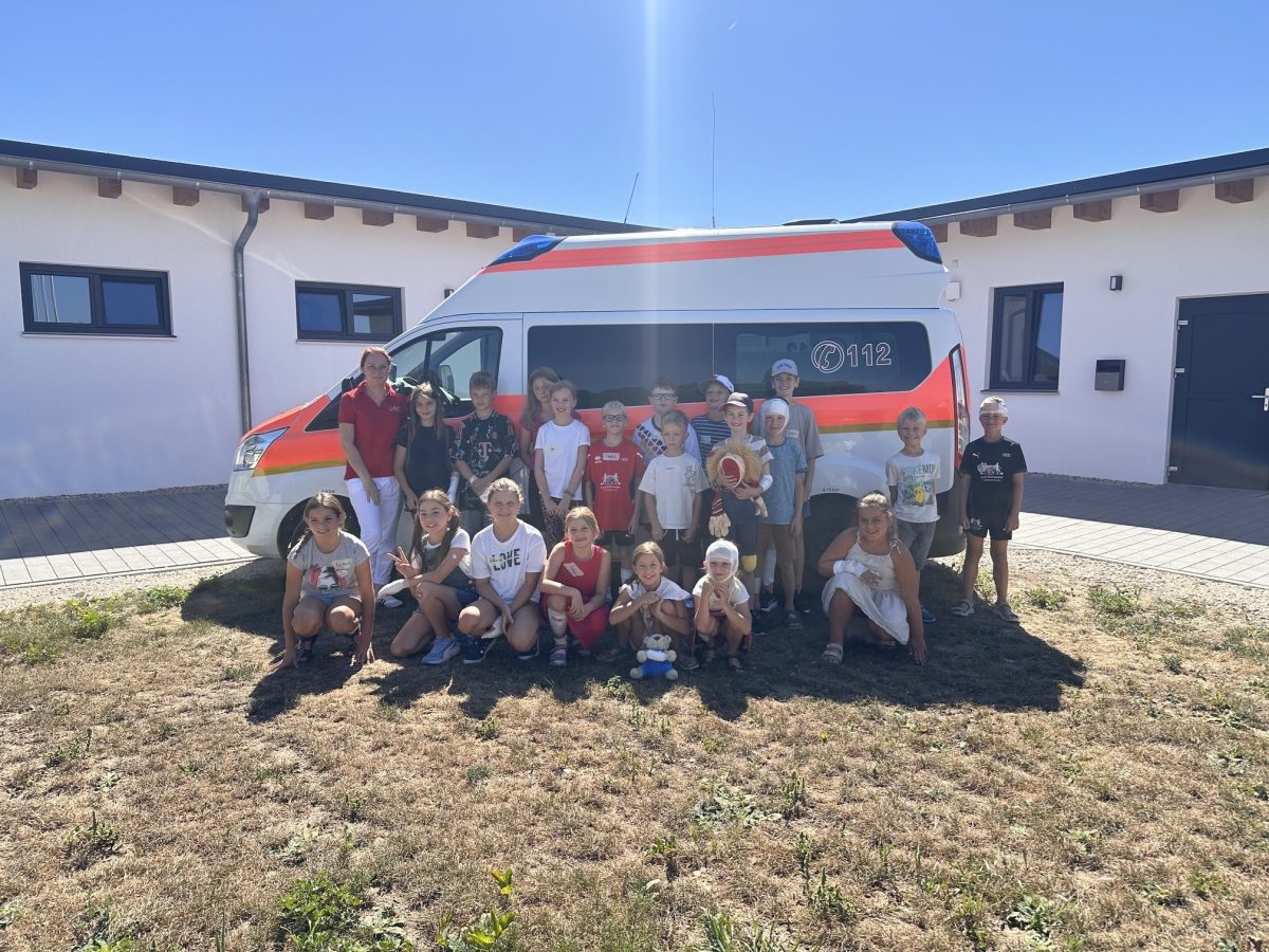 Grundschulkinder und eine Helferin des Bayerischen Roten Kreuzes vor einem Rettungswagen