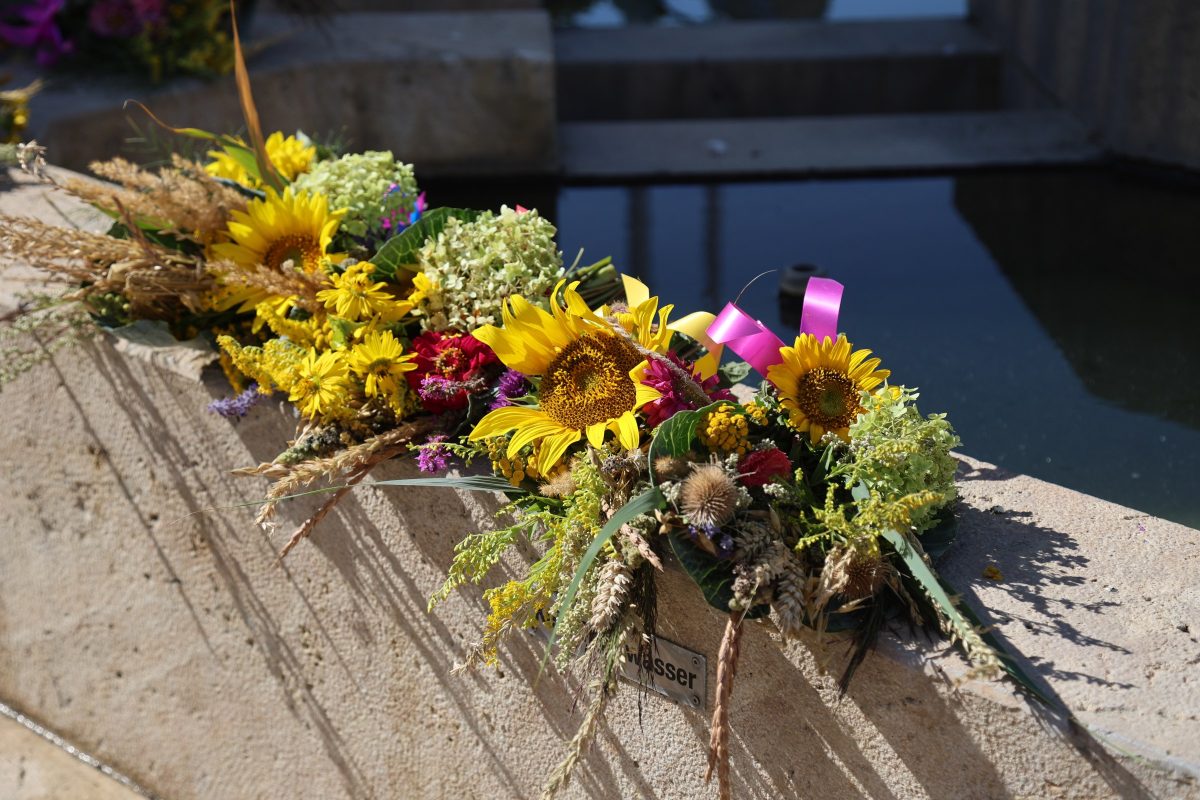 Gebundener Kräuterbüschl mit Sonnenblumen, Getreideähren und Wiesenkräutern auf einem Brunnenrand